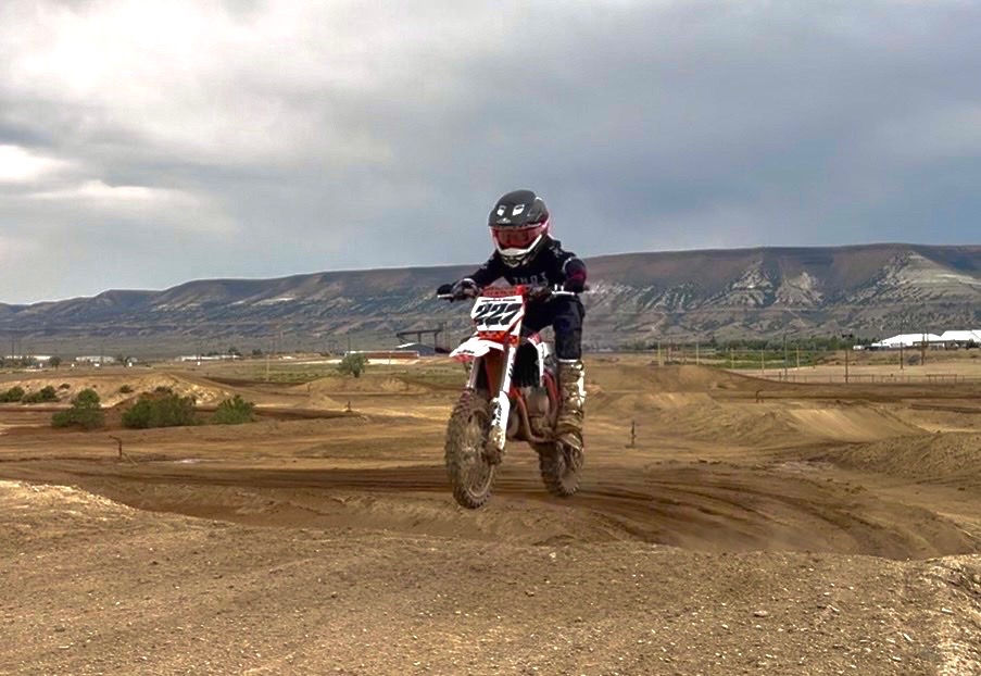 Lincoln Hauk, #227, riding his dirt bike on a motocross track with mesas in the distance.